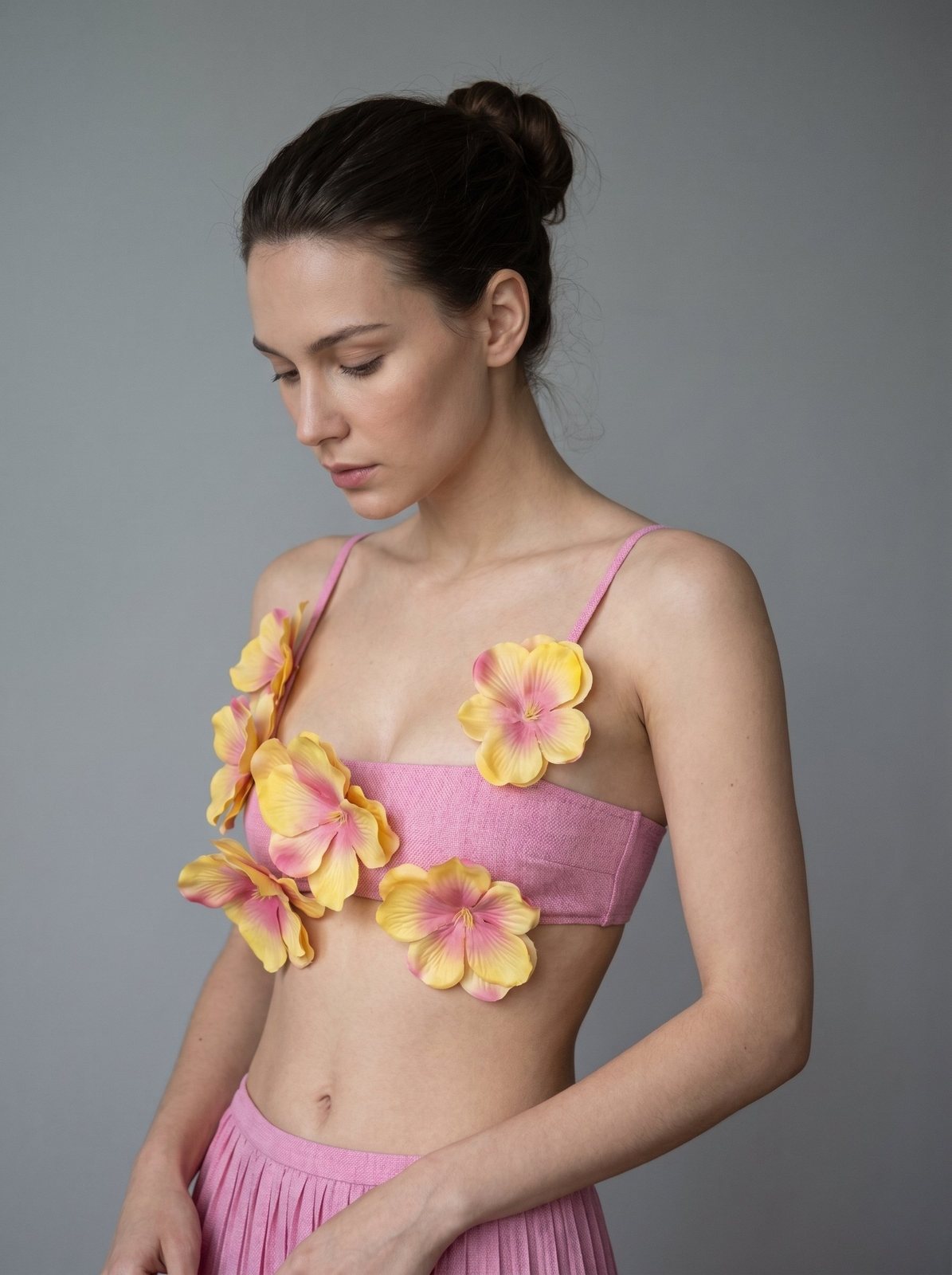 Model in pink crop top adorned with yellow and pink flower appliqués and a pink pleated skirt